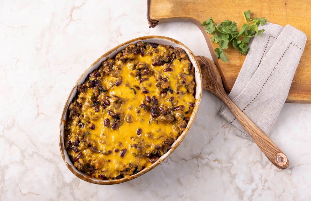 Tamale Casserole in dish with cutting board in the background at overhead view on marble