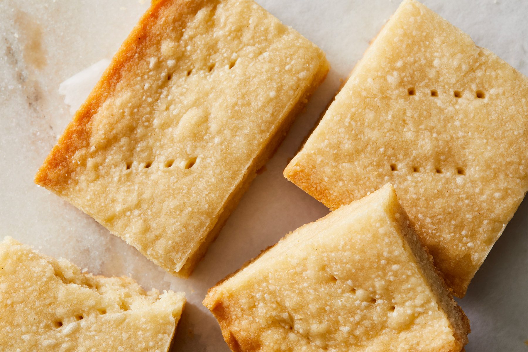 Horizontal Push; close-up of several shortbread cookies arranged on a marble surface, The cookies are square-shaped and have a golden brown color;