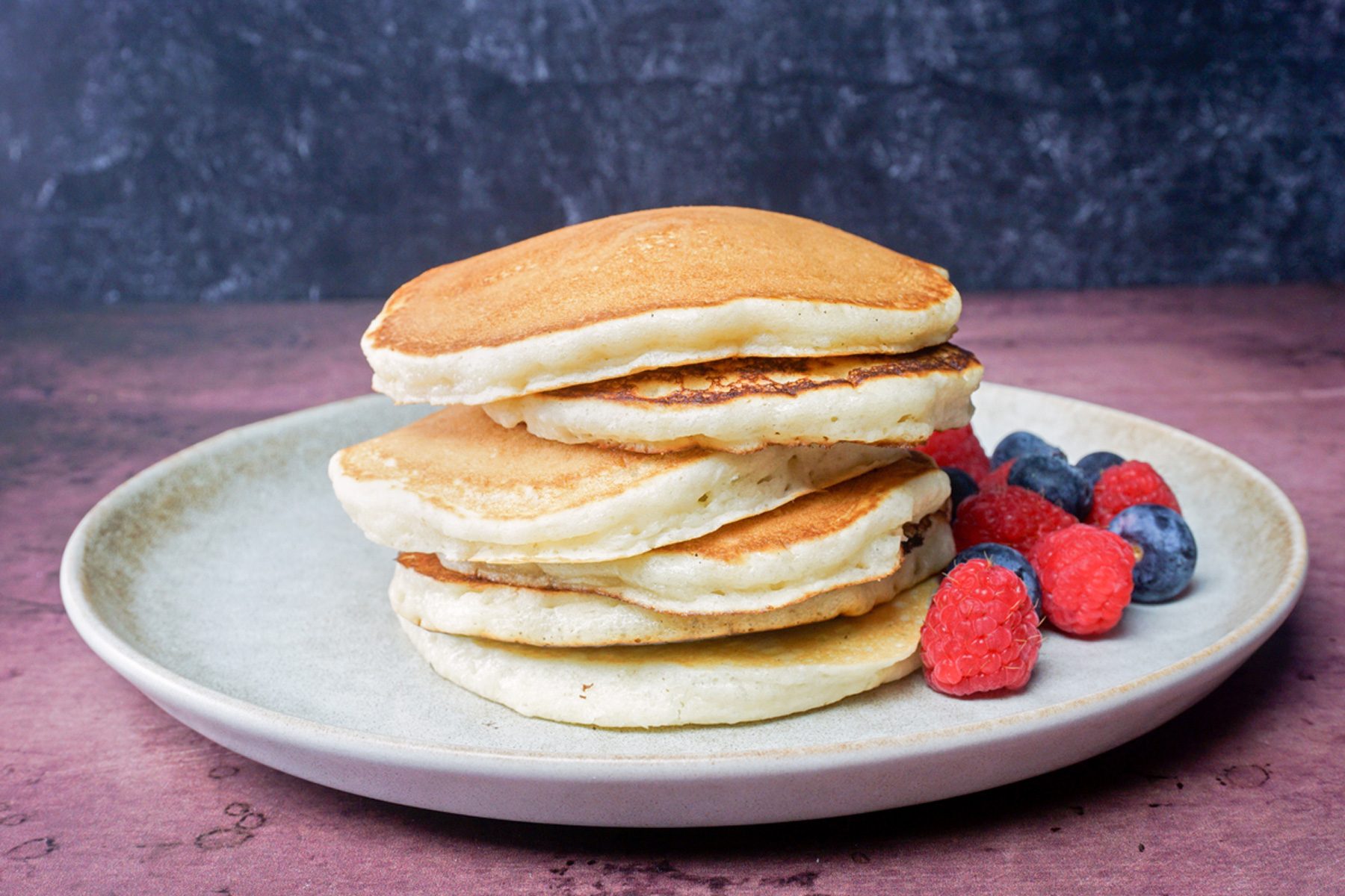 ice cream pancakes stacked with strawberries and blue berries on the side