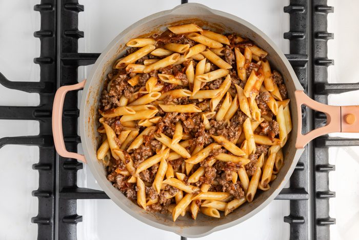 Pasta combined with beef, tomato soup, water and bacon in skillet.