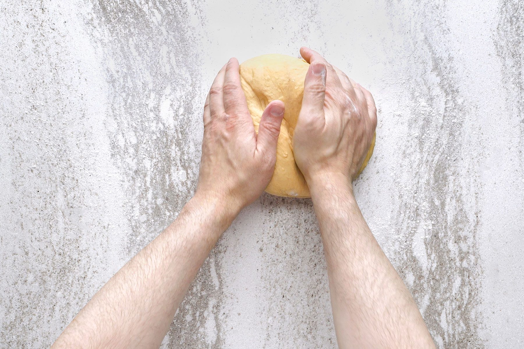 Hands kneading dough on a lightly floured surface.