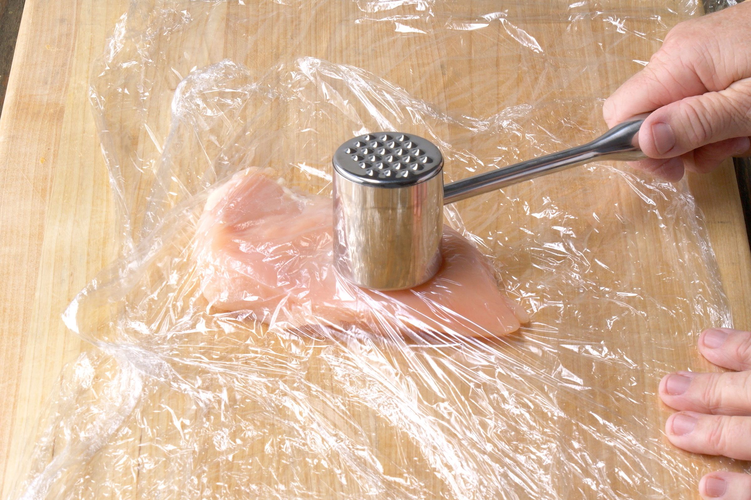 Flattening chicken breast under the plastic wrap by beating it