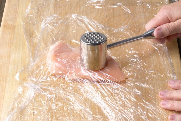 Flattening chicken breast under the plastic wrap by beating it
