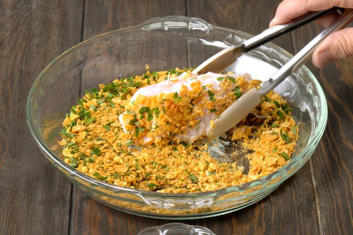 Dipping buttermilk coated chicken breast roll in cornflakes mixture