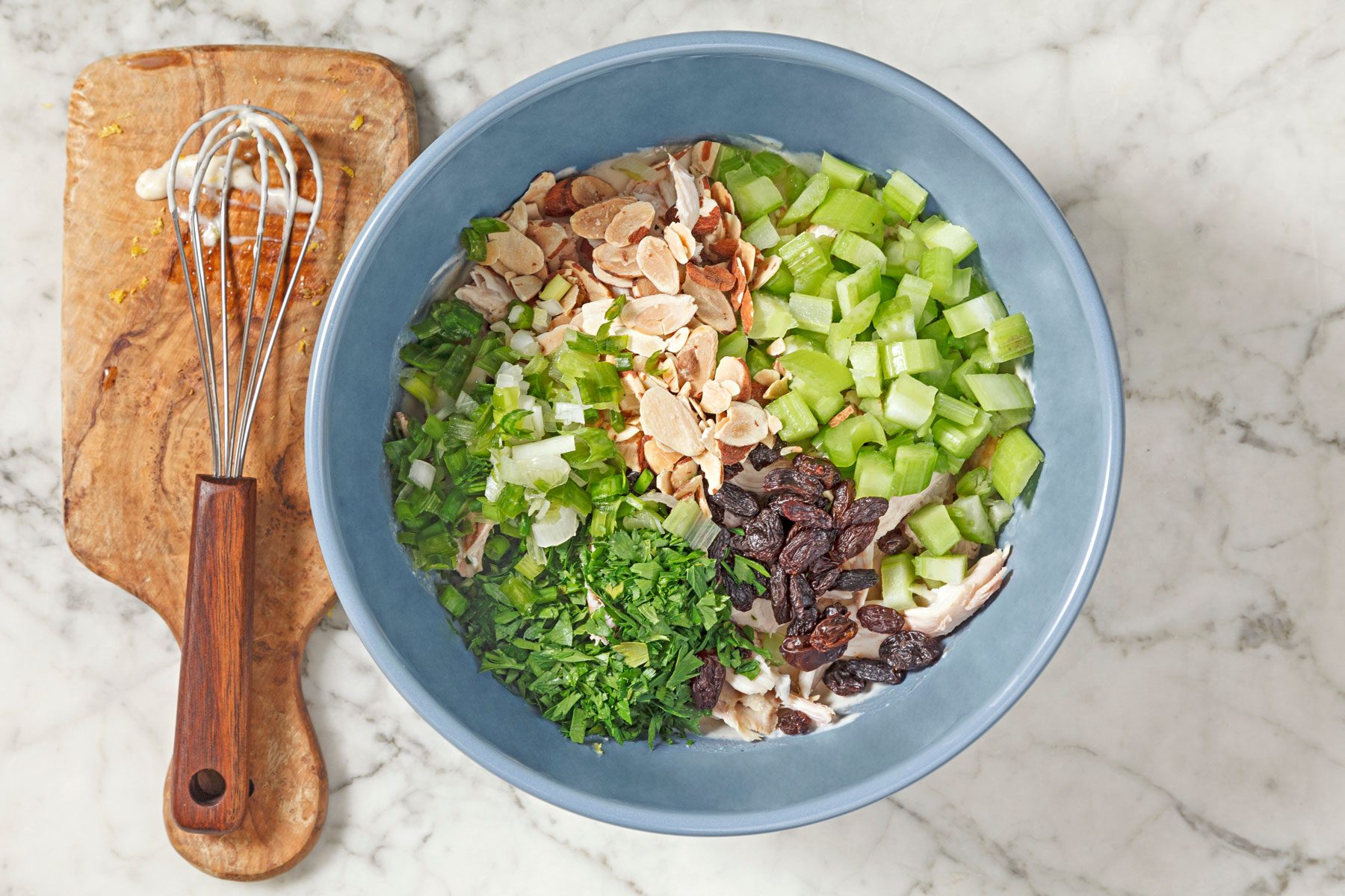 shredded cooked chicken, celery, green onion, parsley, raisins and almonds in a bowl
