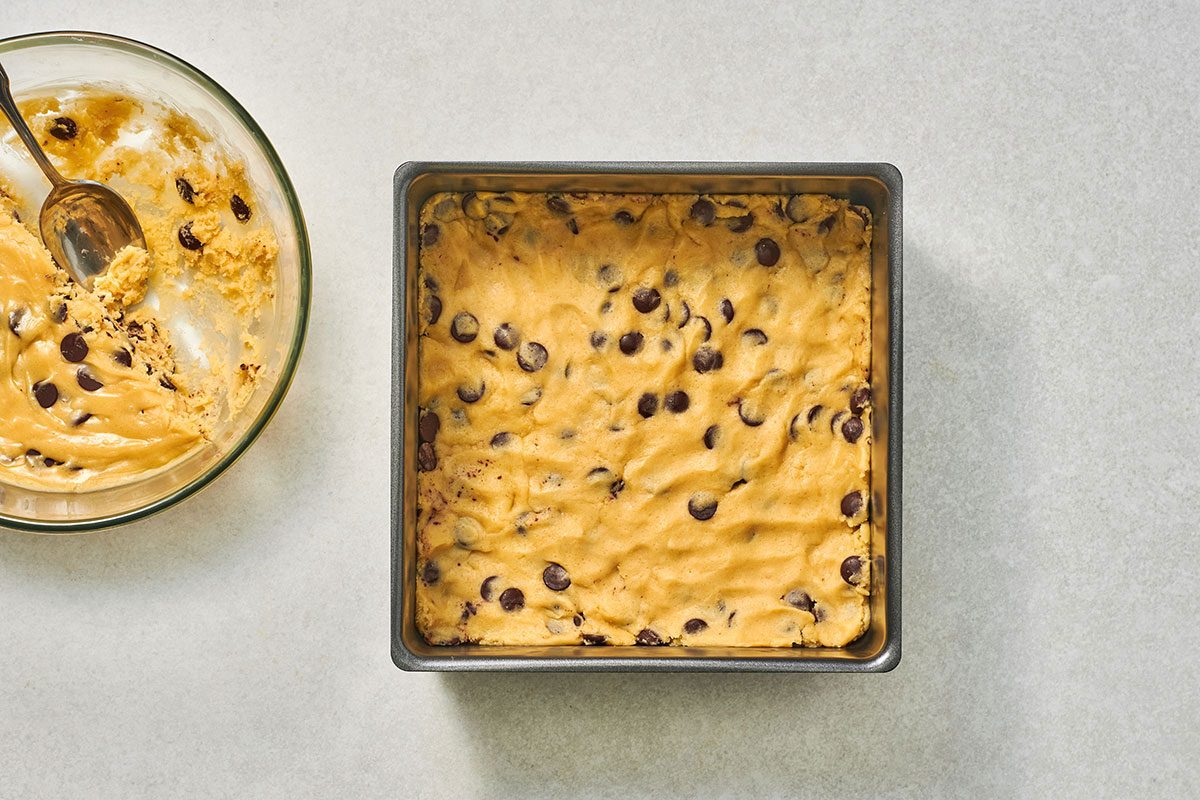 Half of the cookie dough pressed into the bottom of a square baking pan