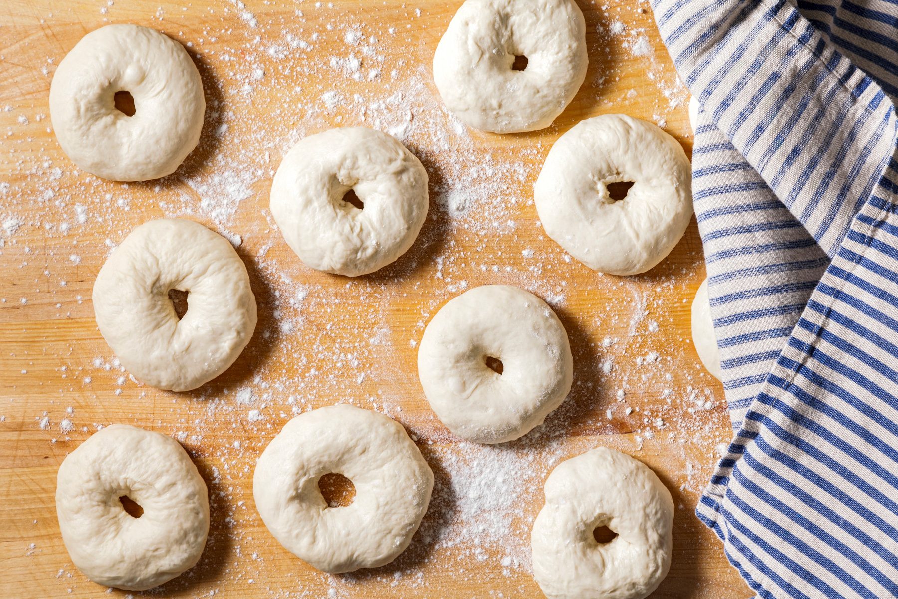 Overhead shot of placing dough on a floured wooden surface, covering with kitchen towels, and letting rest for 10 minutes.