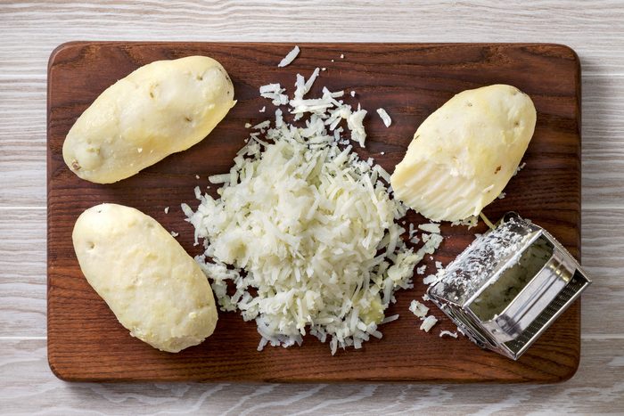 Shredding of peeled potatoes with a grater on a wooden board