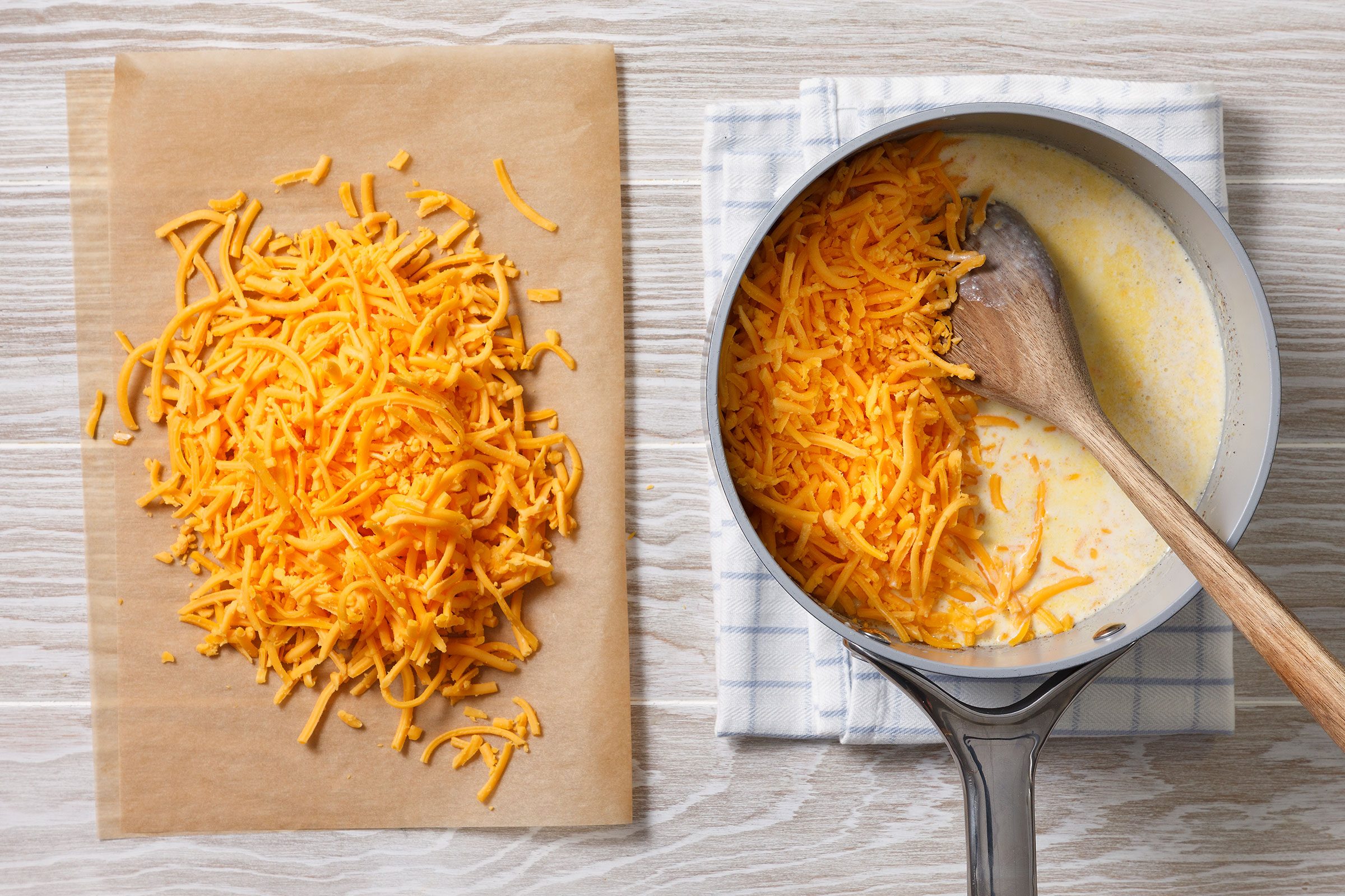 Shredded cheese on one side and a saucepan with cream sauce and shredded cheese in it