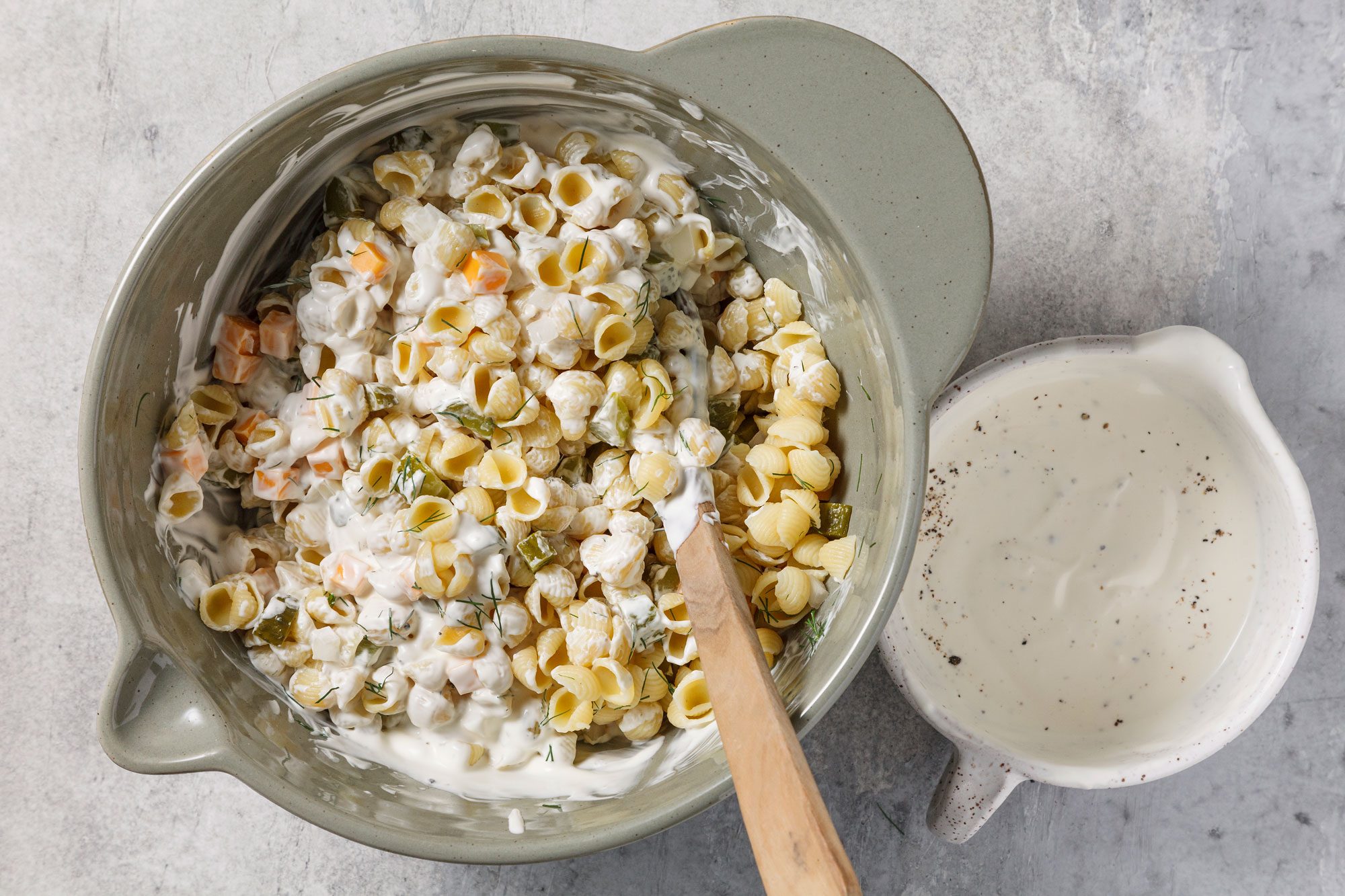 Overhead shot of stir into pasta mixture; refrigerate; covered at least 1 hour before serving; wooden spoon; grey surface;
