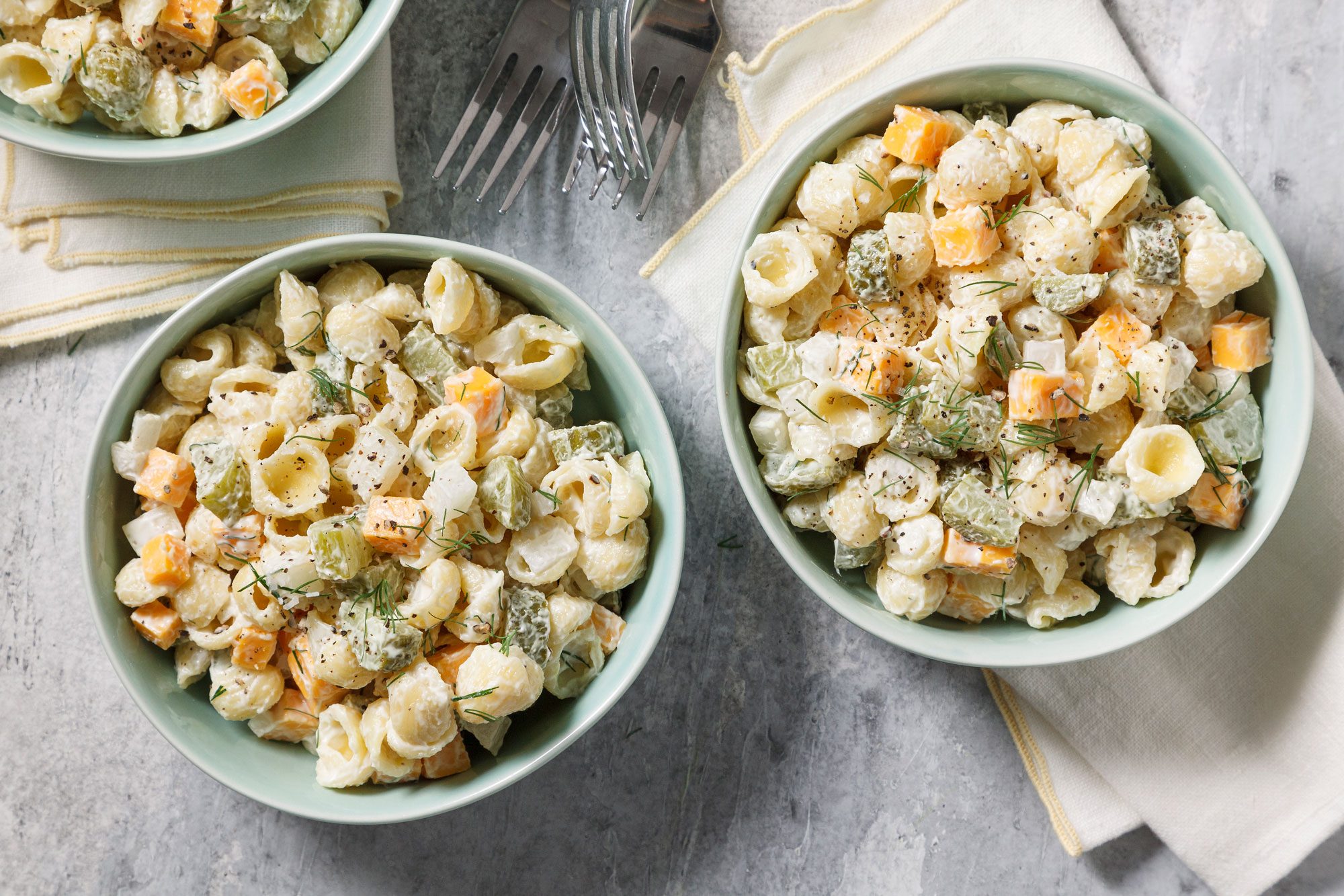 Top view shot of Dill Pickle Pasta Salad; serve in bowls; forks; napkins; grey surface;