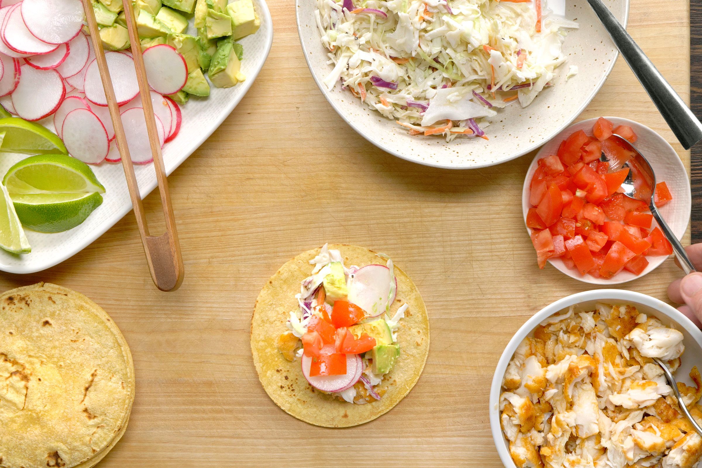 Filled taco with filapia and coleslaw with all the ingredients for fish taco on side