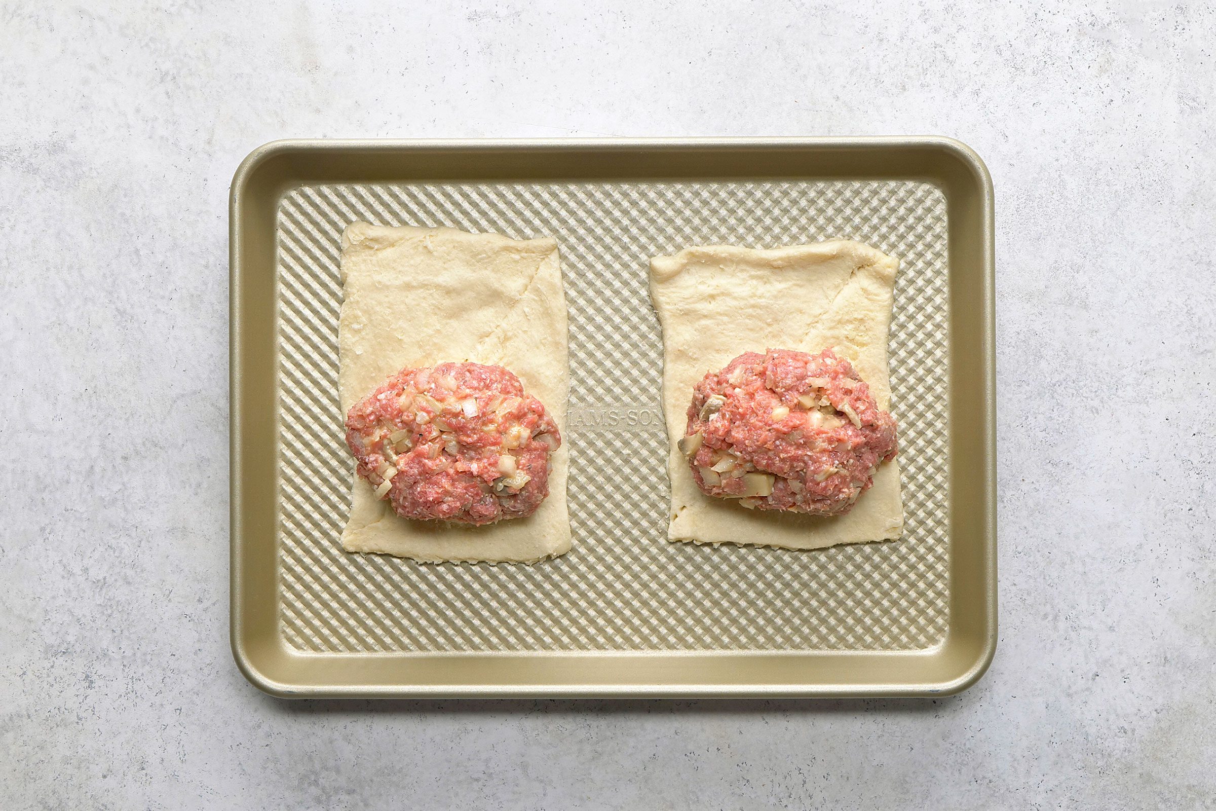 Beef and egg mixture balls separated in two halved and spread on rectangular dough sheets