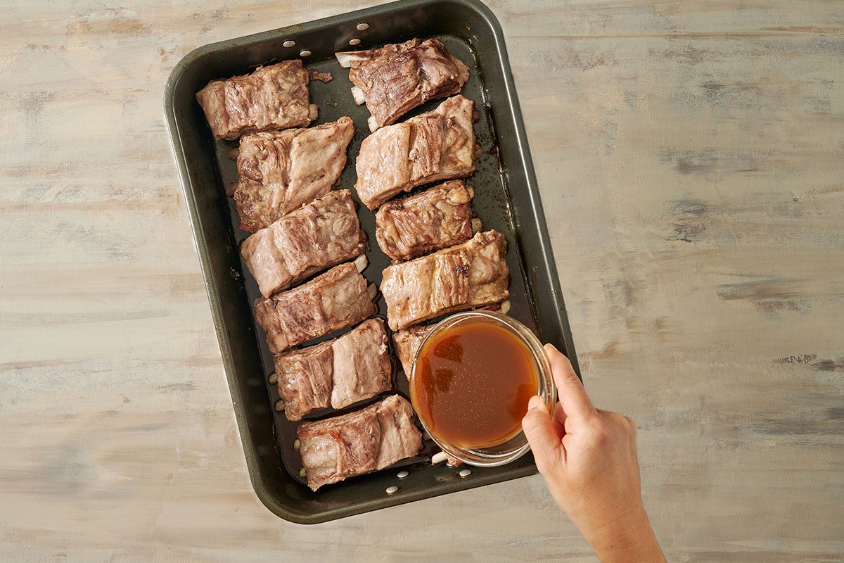 Overhead view of ribs being coated with honey garlic sauce in a roasting pan, ready to bake uncovered for the Taste of Home Honey Garlic Ribs recipe.
