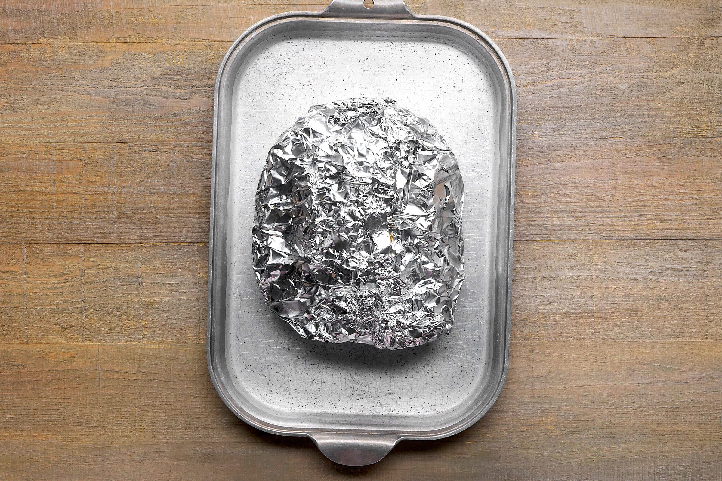 Pork meat wrapped in foil and placed on a shallow baking pan