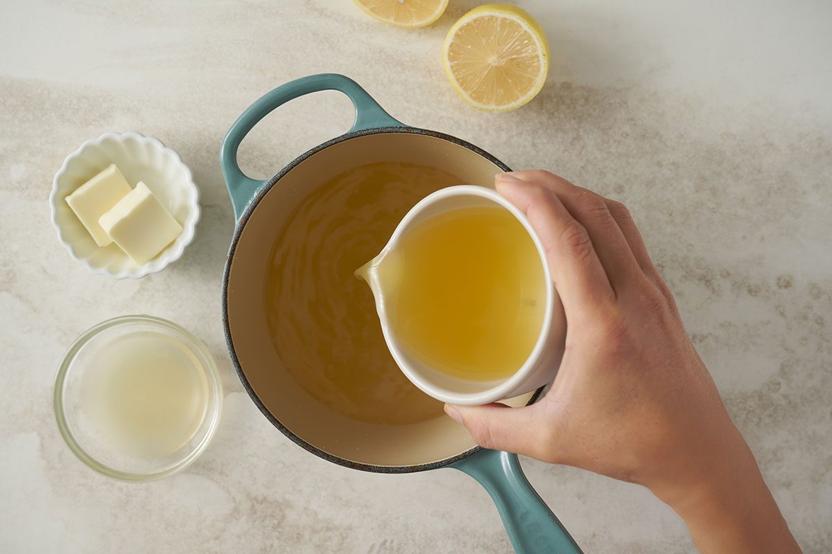 Overhead view of the lemon rice liquids—chicken broth, lemon juice, butter, and water— in a saucepan for the Taste of Home Lemon Rice recipe