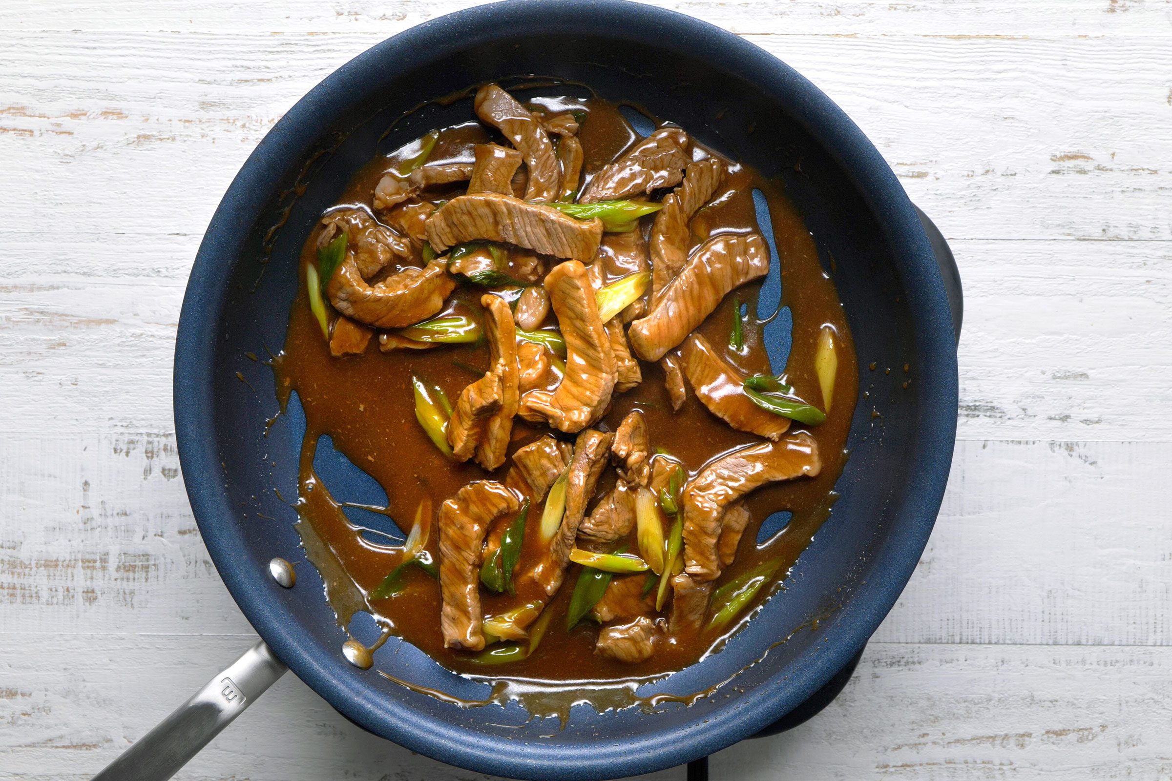 Beef mixed with sauces and onions in a large skillet