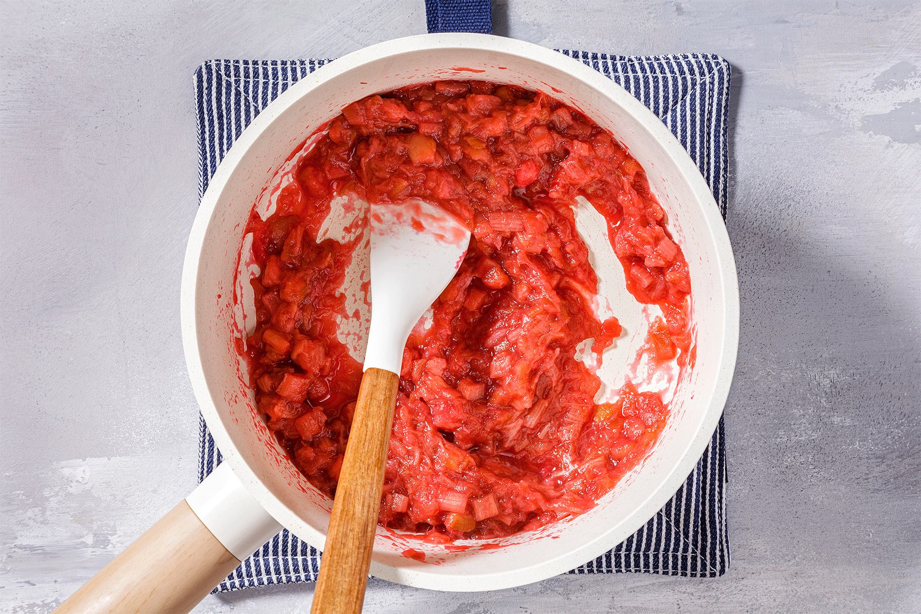 Overhead shot of same saucepan; reduce heat; simmer uncovered 10-15 minutes or until rhubarb is tender; stirring occasionally; spatula; napkin; grey surface;