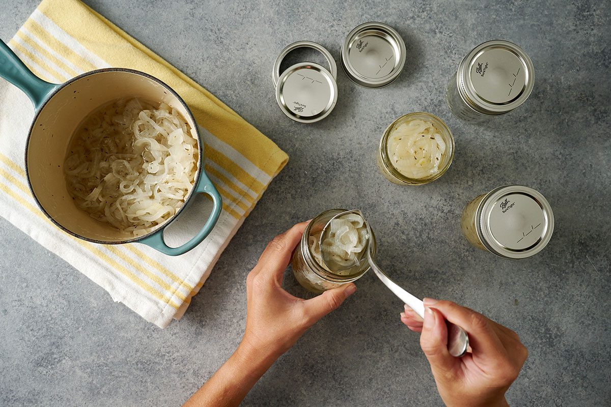 Overhead view of the hot onion mixture being carefully ladled into hot half-pint jars, with proper headspace being maintained for the Taste of Home Pickled Sweet Onions recipe.