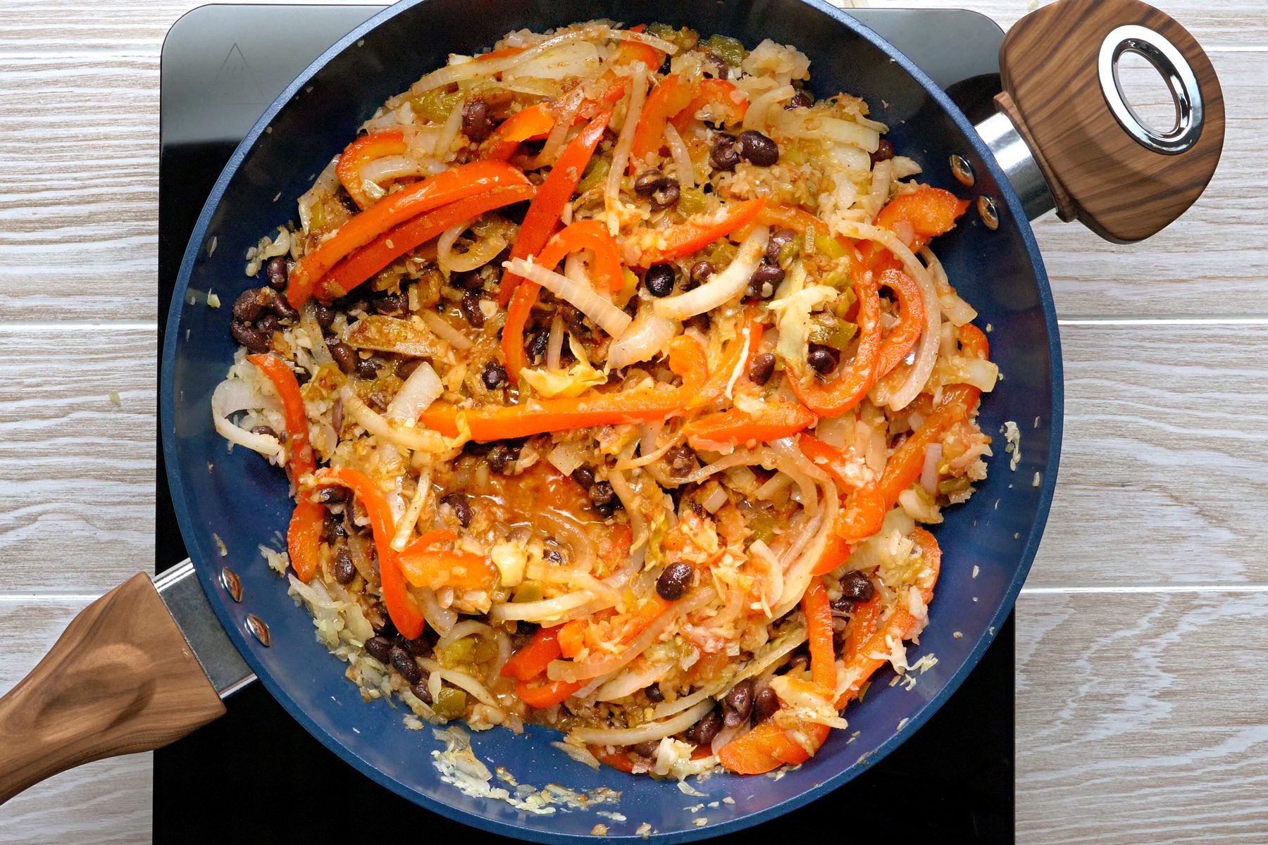 A variety of vegetables and beans cooking in a skillet.