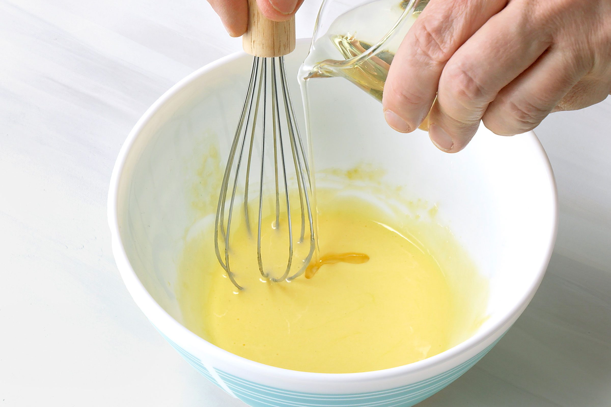 Adding oil drop by drop into egg yolks mixture in a bowl