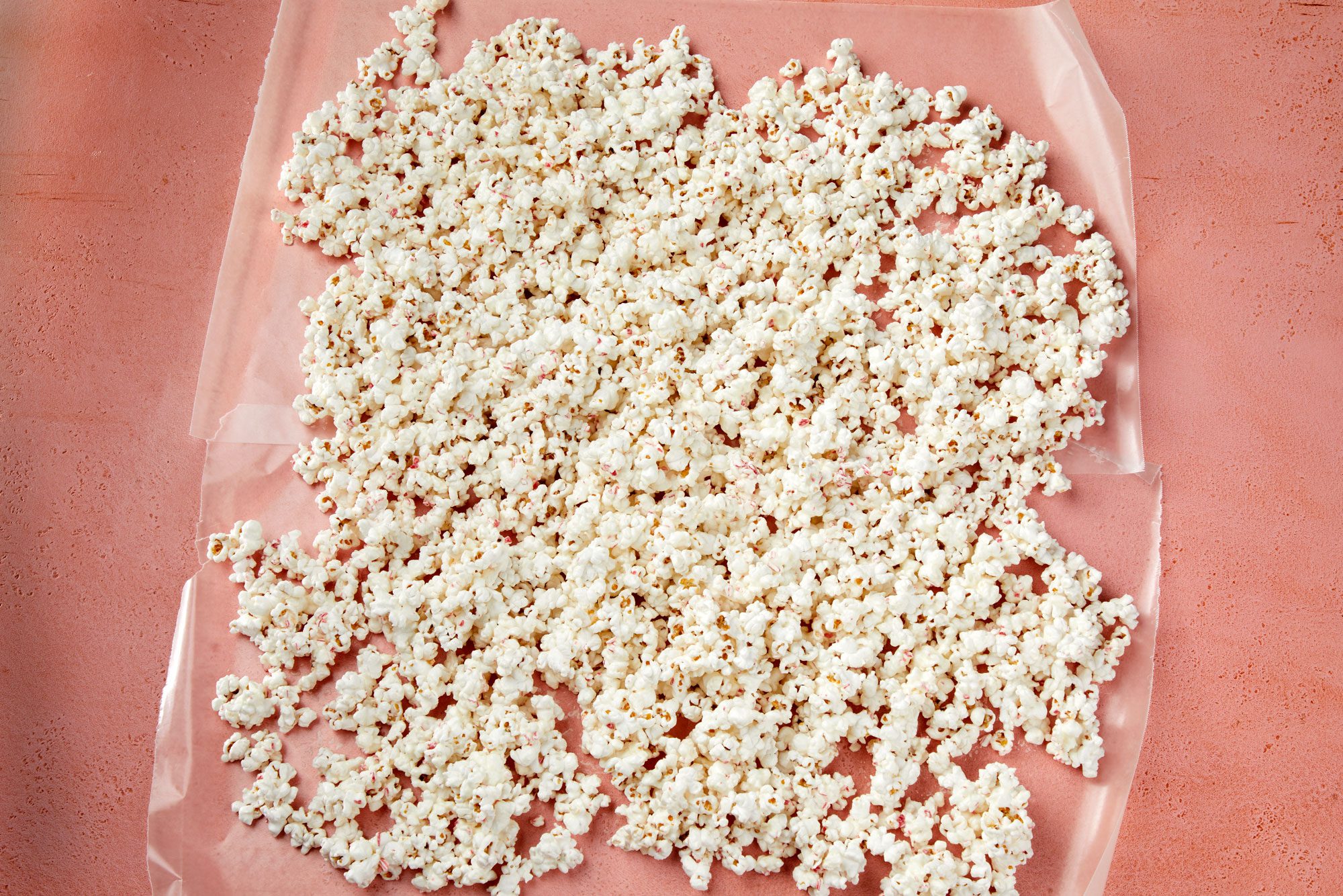 overhead shot of popcorn onto a waxed paper-lined baking sheet over pink background;