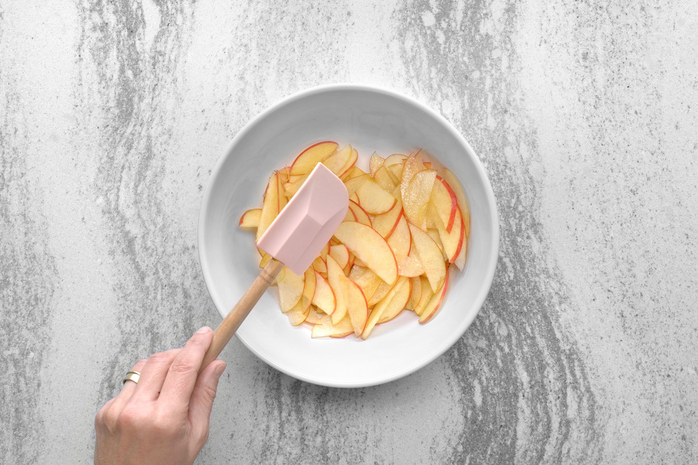 Apple slices and lemon juice in a large bowl with a hand holding a ladle