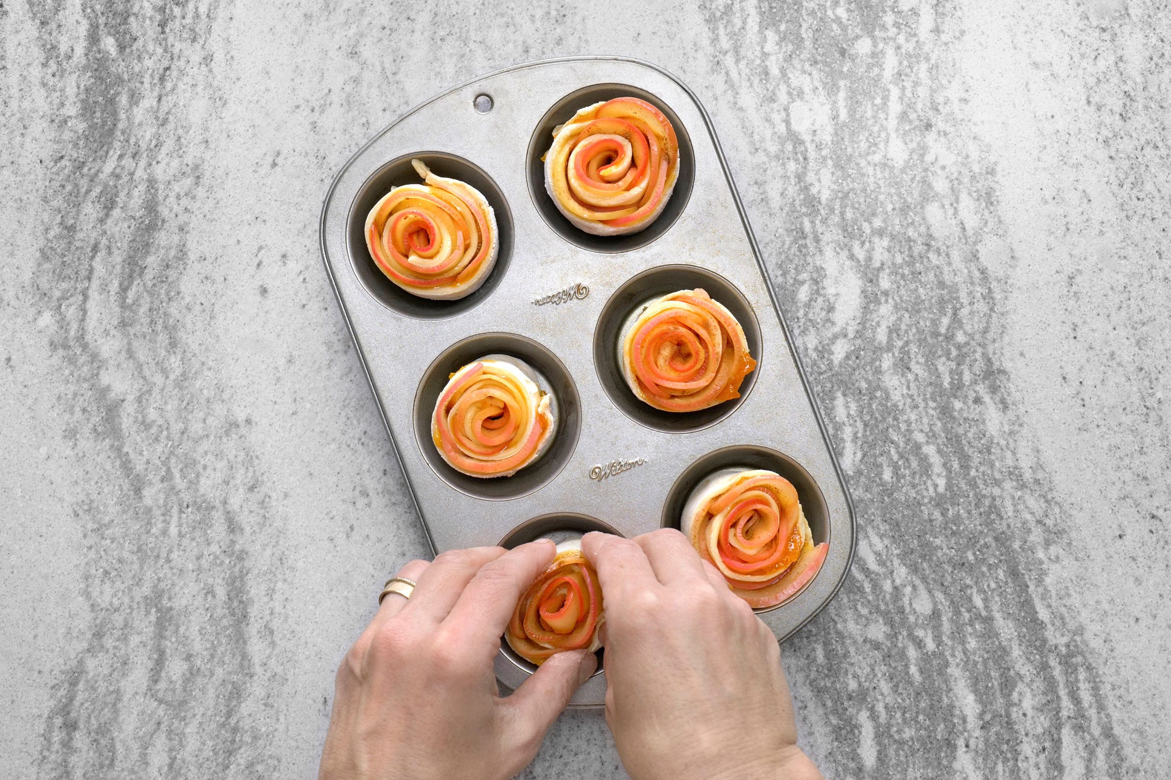 Puff pastry with apple slices rolled into rose shape in baking muffin tins