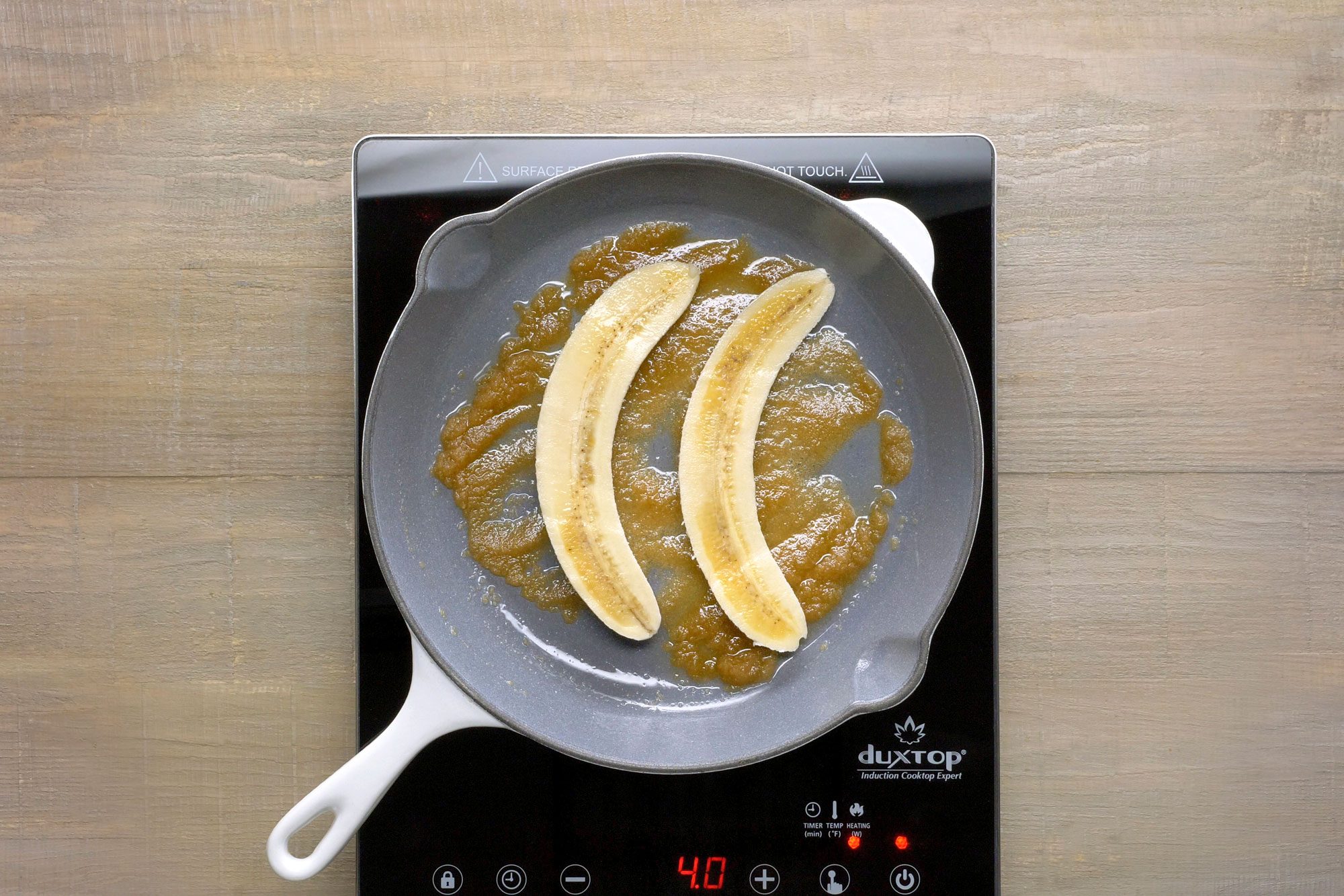 A cast iron skillet on an induction stovetop, the skillet contains two banana halves that have been caramelized in brown sugar