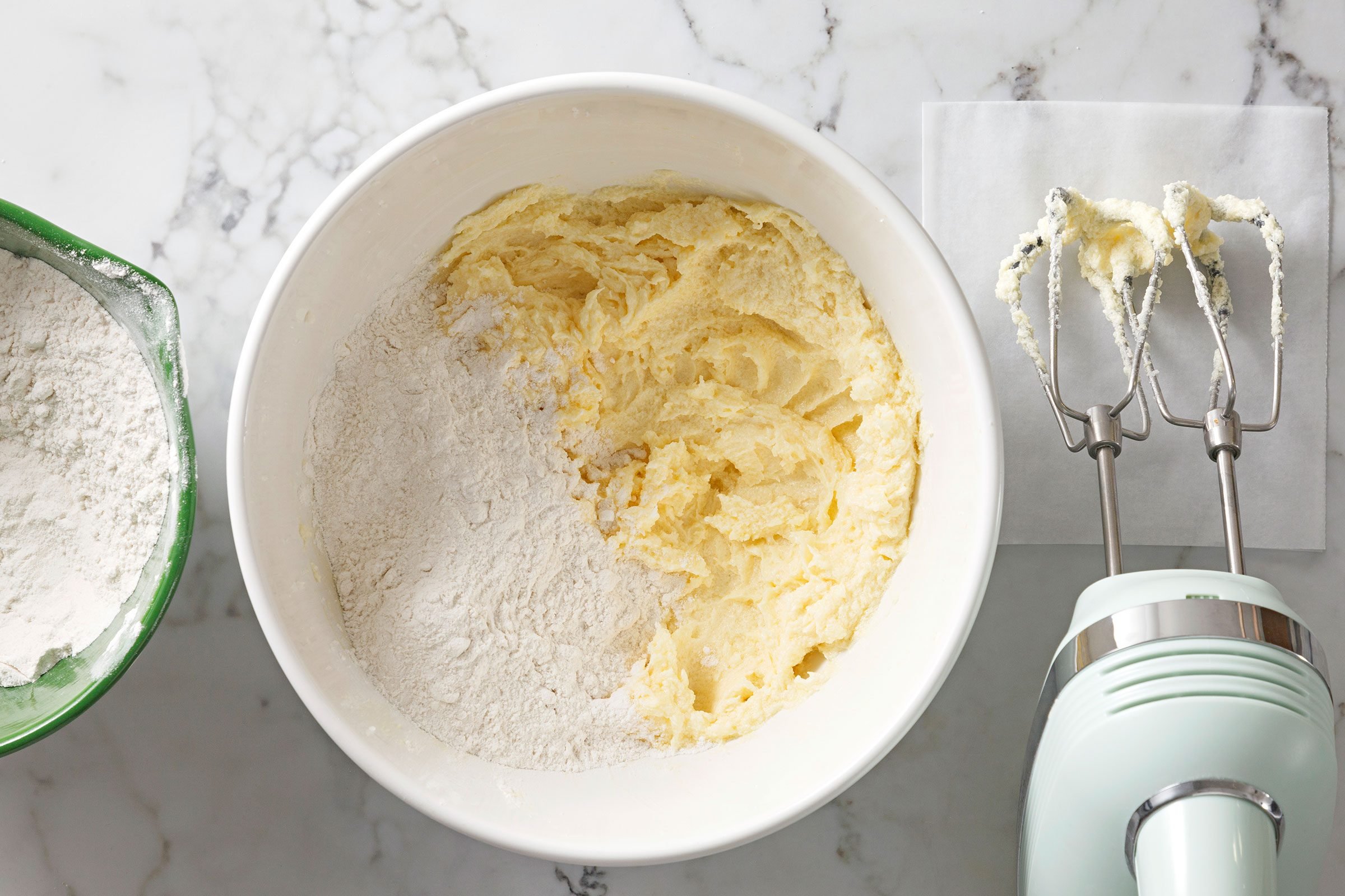 Flour added to creamed butter mixture in a large bowl with blender on side