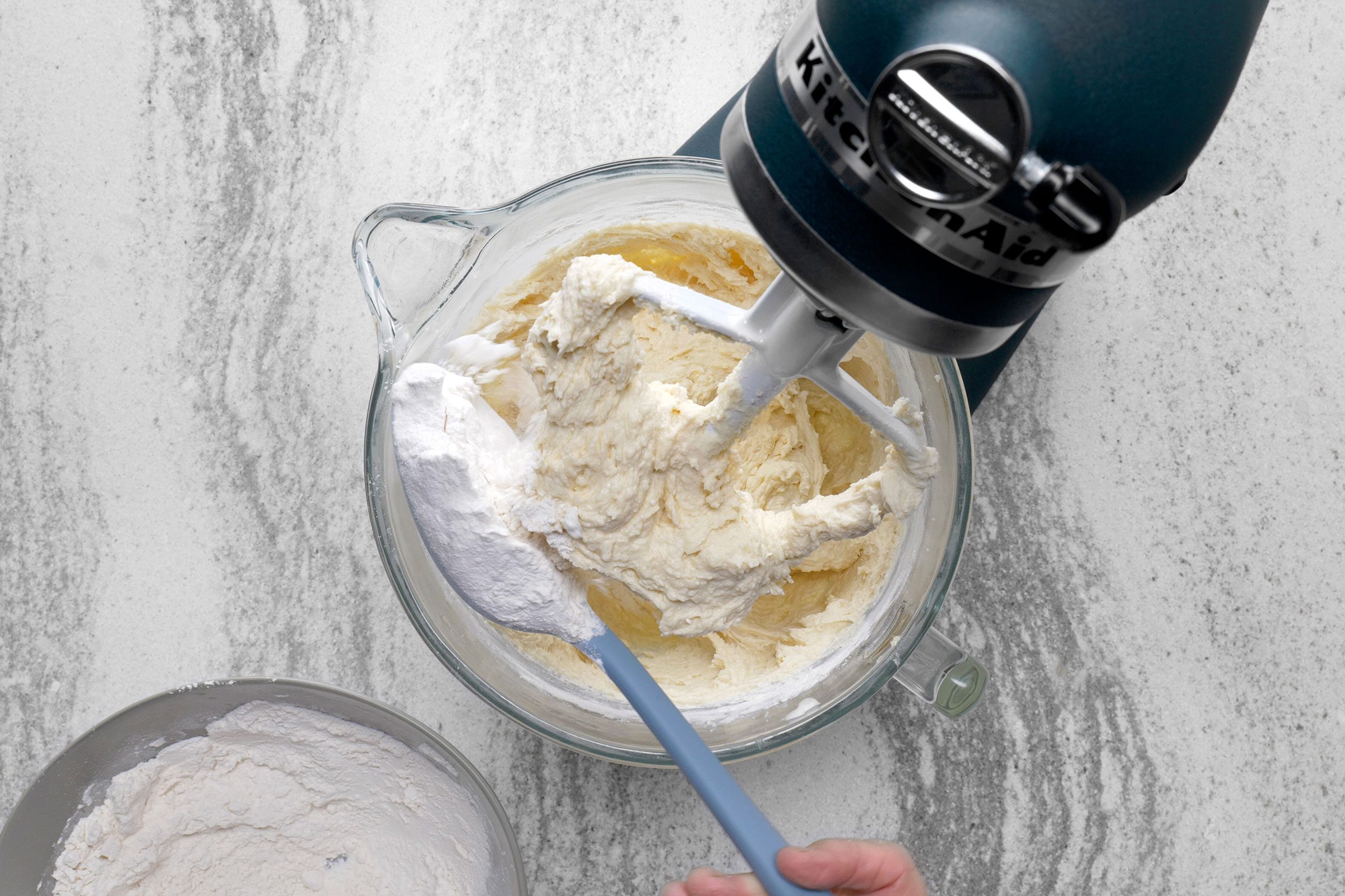 Flour added using a serving spoon to the butter, sugar and cream mixture in a large bowl