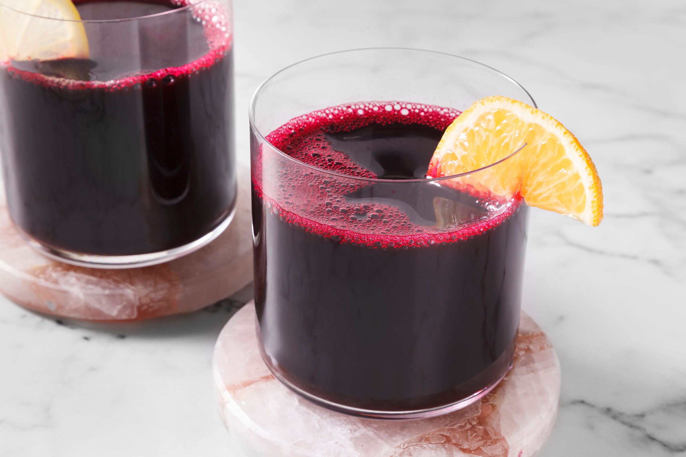 Beet Juice in glasses on top of coasters with a lemon slice on the rim of the glass