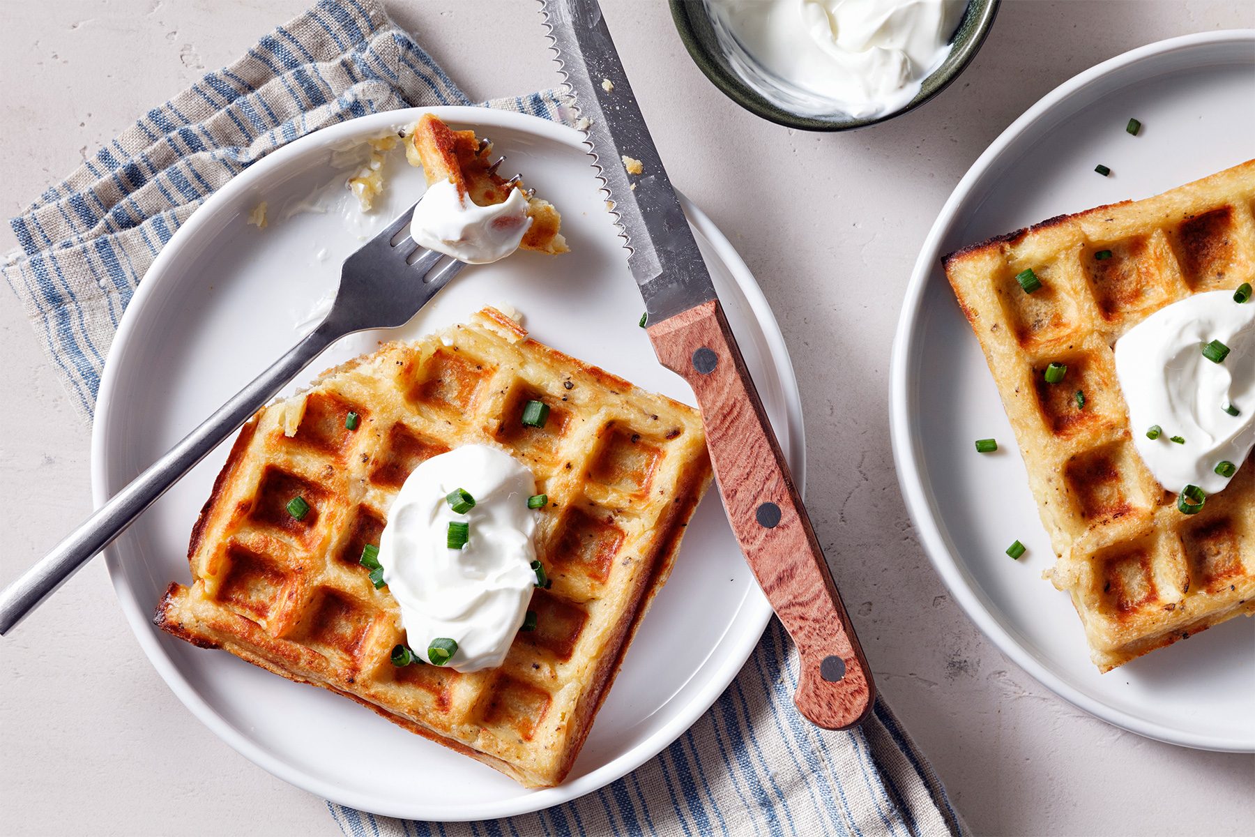 overhead shot of mashed potato waffles topped with sour cream and minced chives