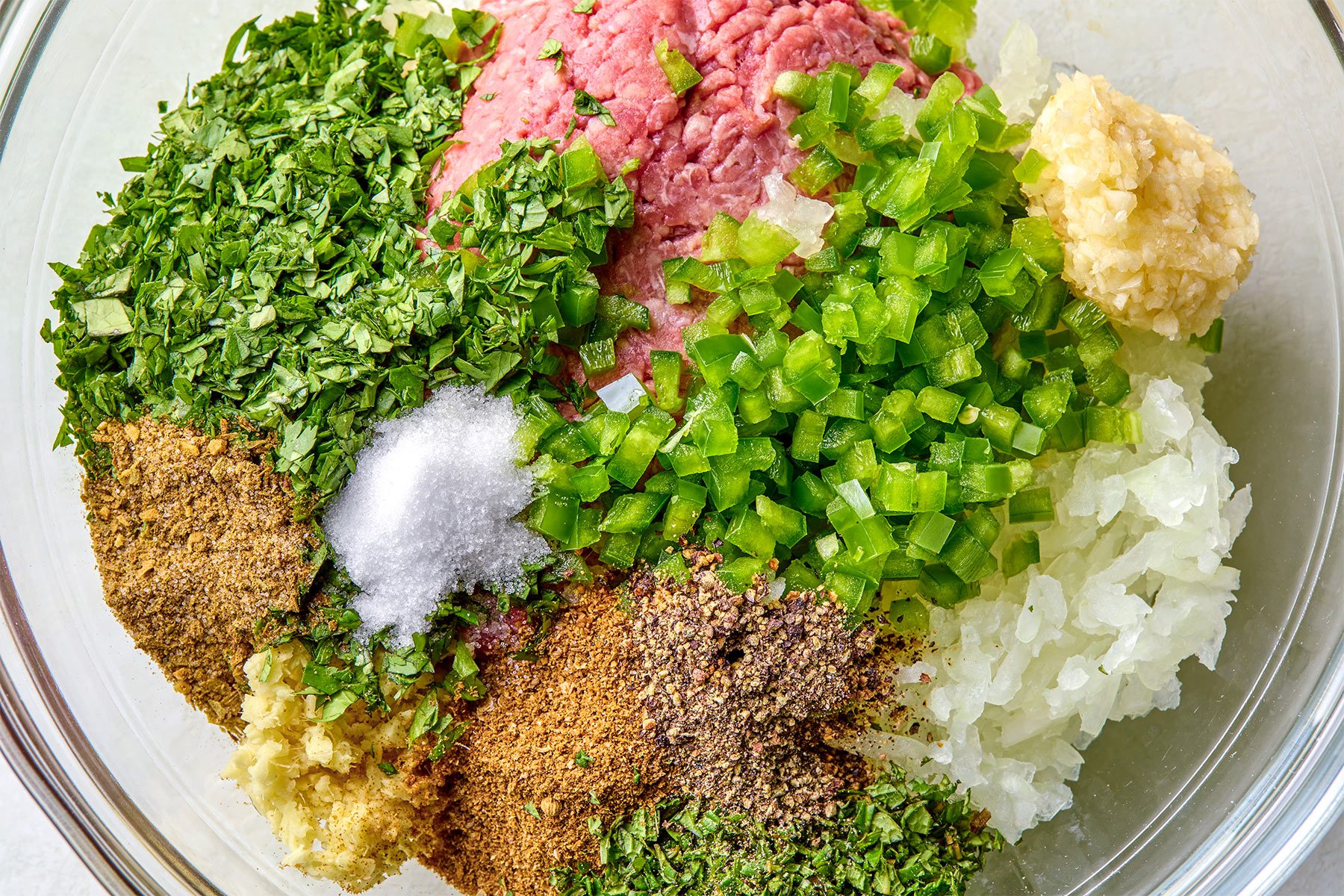 overhead shot of a large bowl, combined ground beef, onion, jalapeno, garlic, ginger, cilantro, mint, ground cumin and coriander, salt, pepper, garam masala and ground cumin and coriander seeds; mix well
