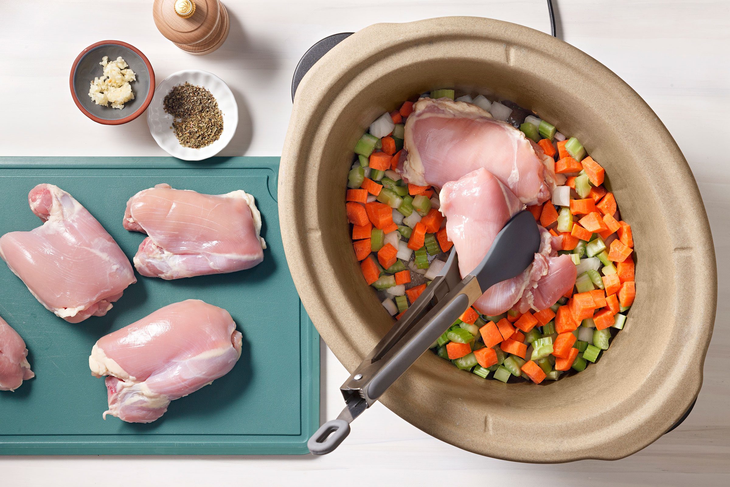Placing chicken on top of chopped vegetables in a cooker with seasoning on the side