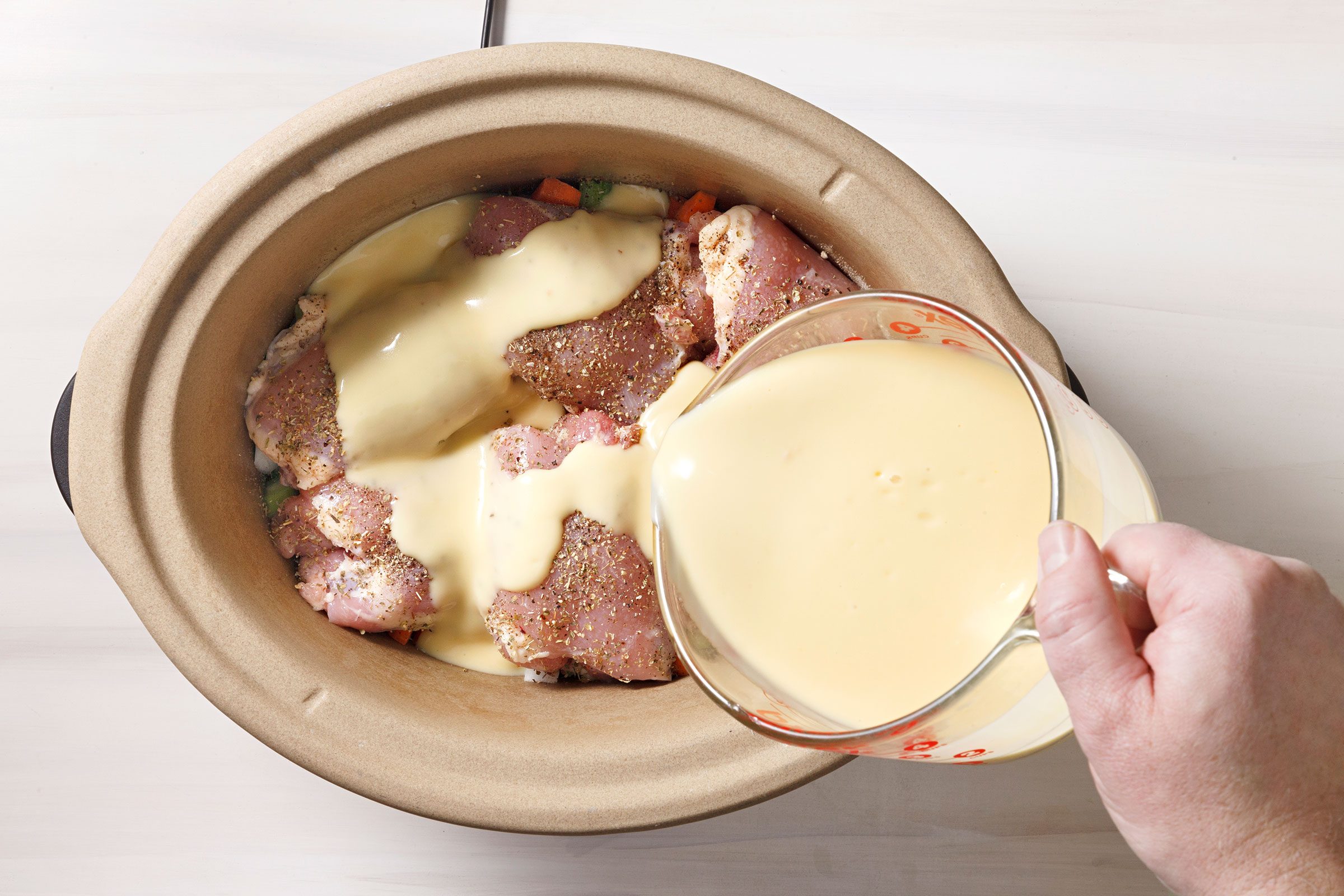 Pouring chicken soup and broth mixture on top of chicken and chopped vegetables