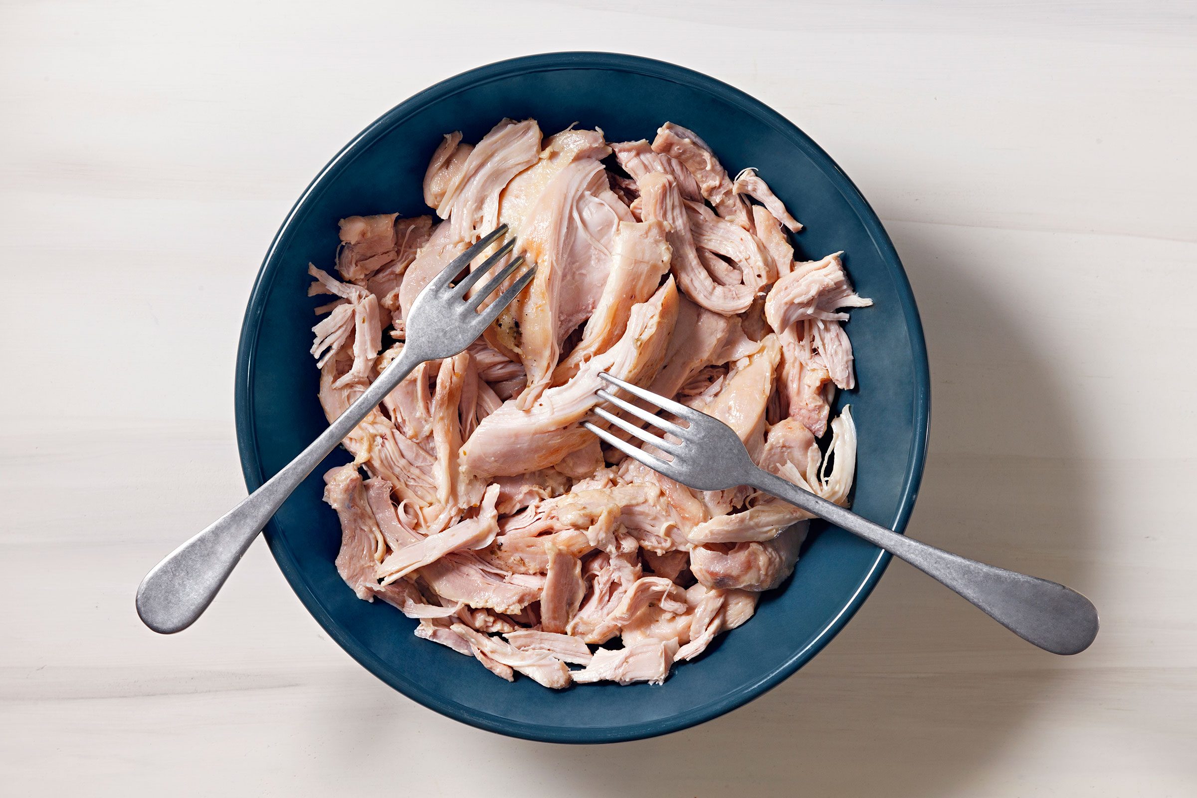 Shredded chicken using two forks in a blue bowl