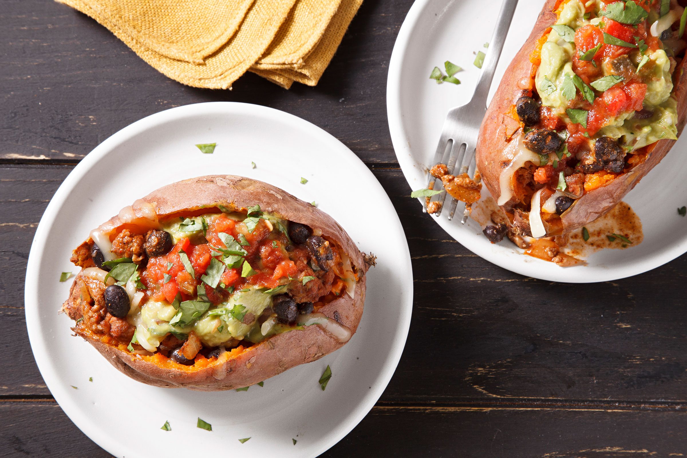 Stuffed Sweet Potatoes served on white plates with guacamole, salsa and cilantro on top
