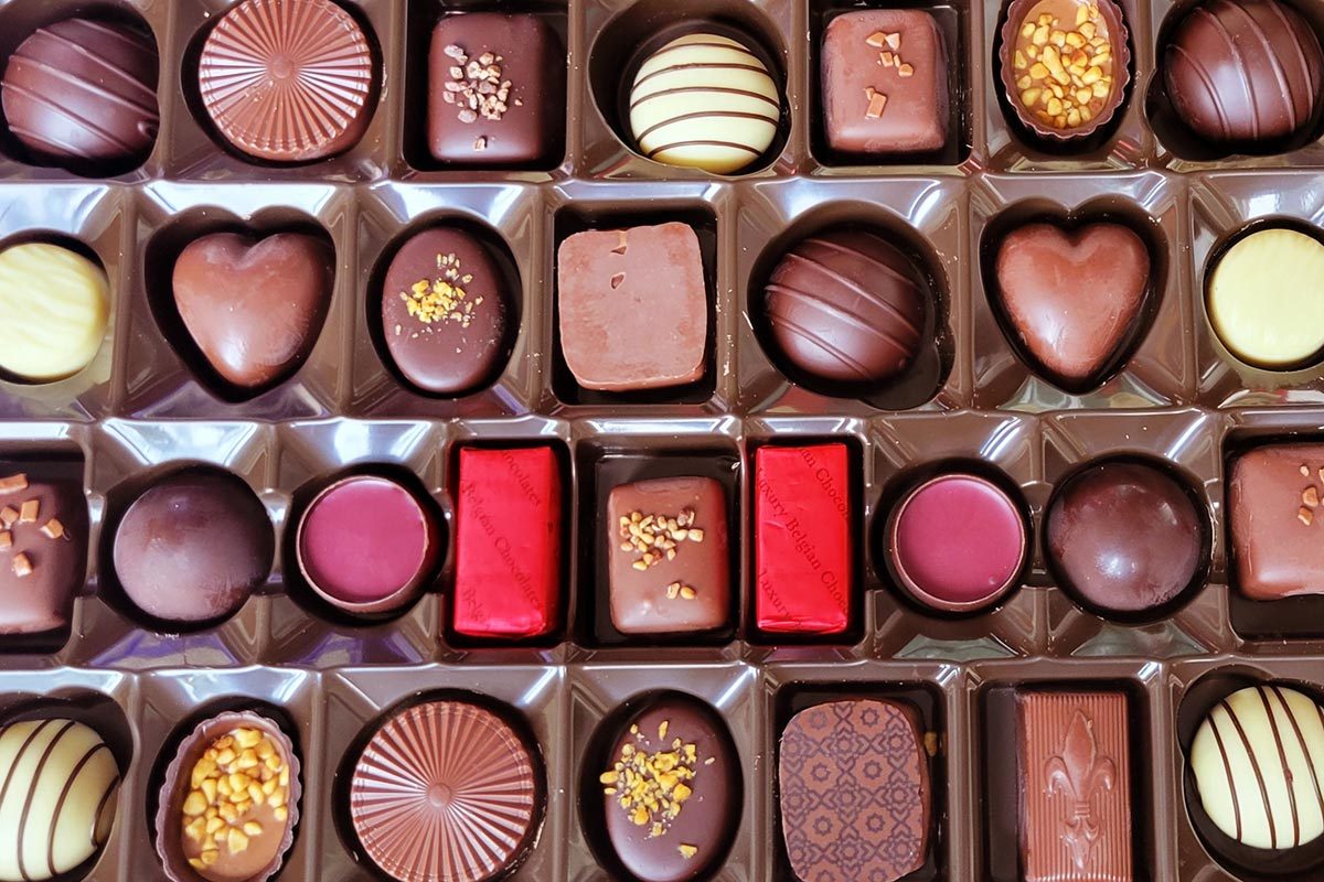 An array of different colored chocolate truffles sit snugly in a brown chocolate box
