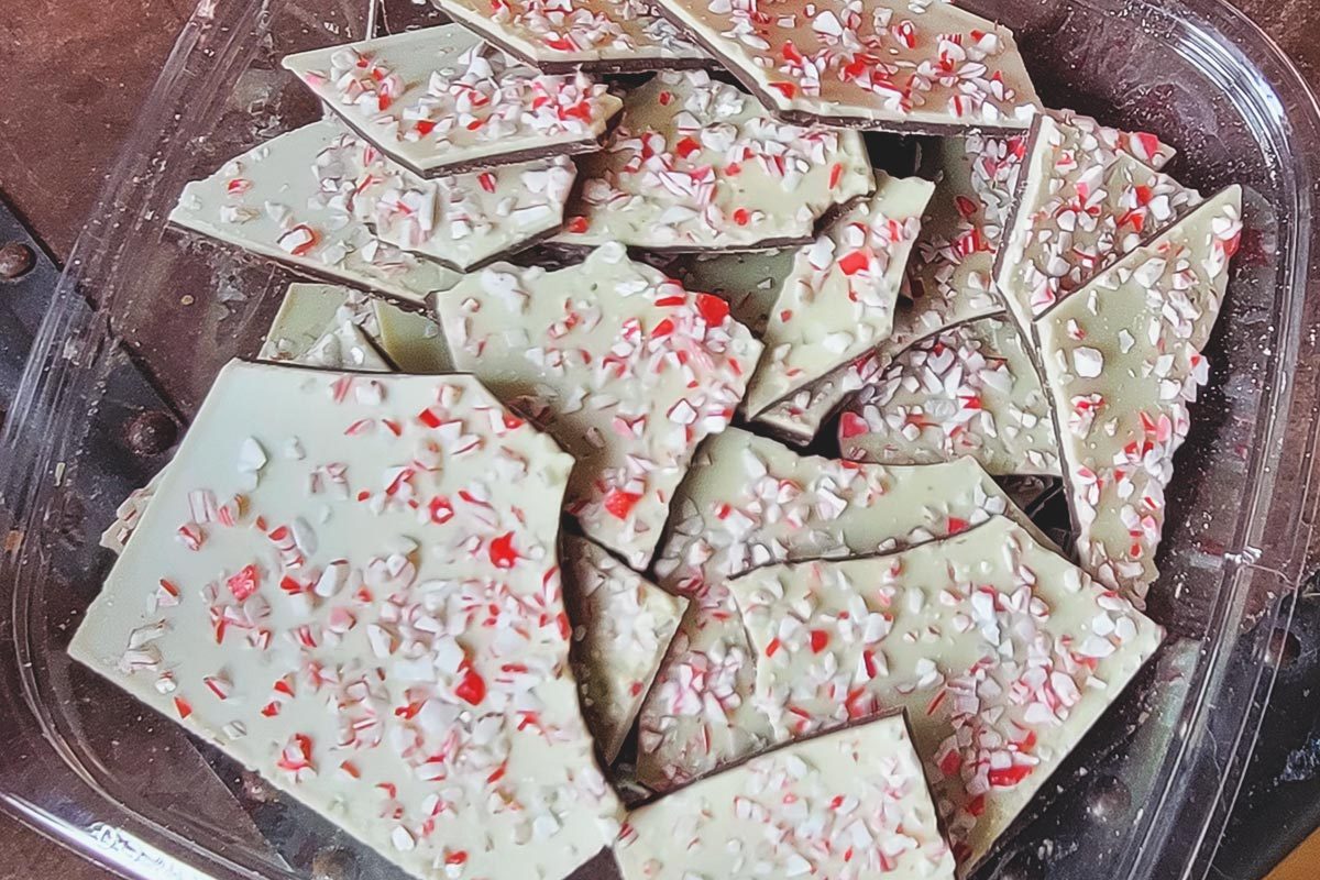 Shards of white peppermint bark, topped with pieces of crushed red-and-white peppermint, in a plastic container