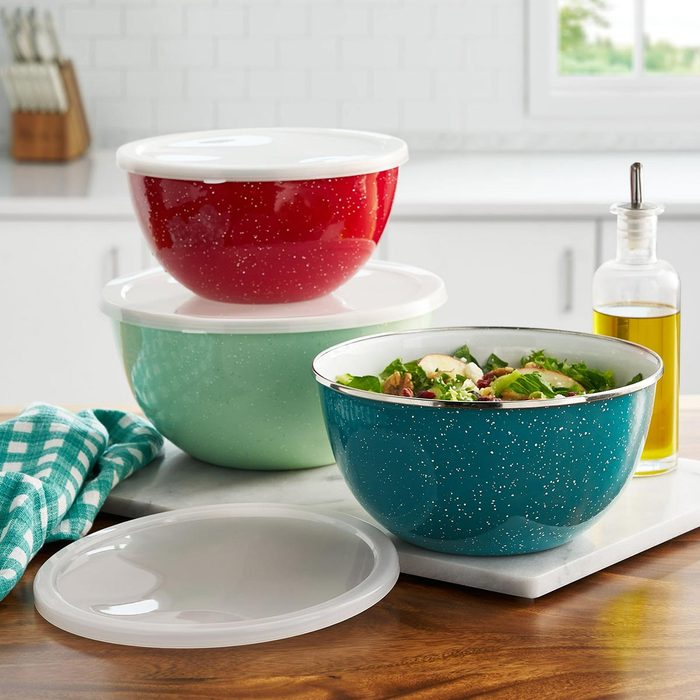 A set of multicolored enamel mixing bowls on a counter with a bottle of olive oil in the background