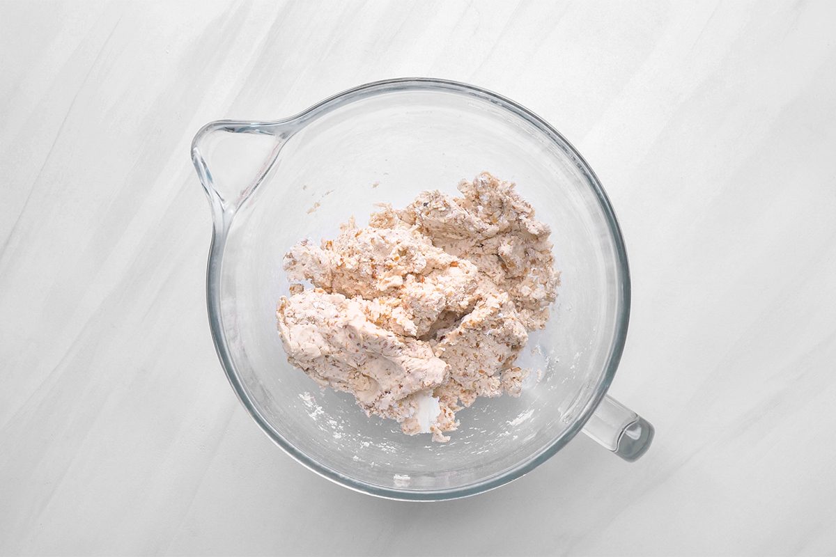 A glass mixing bowl containing a mixture of flour and dry ingredients on a light marble surface.