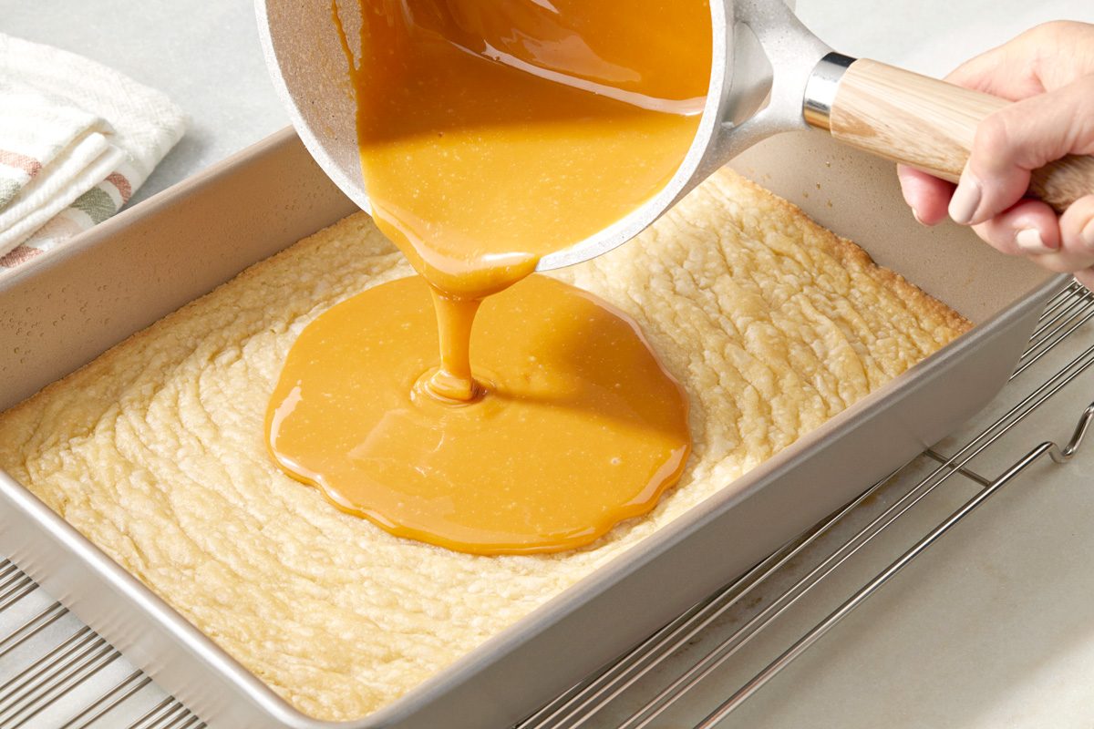 caramel and cream mixture being poured over cookie crust