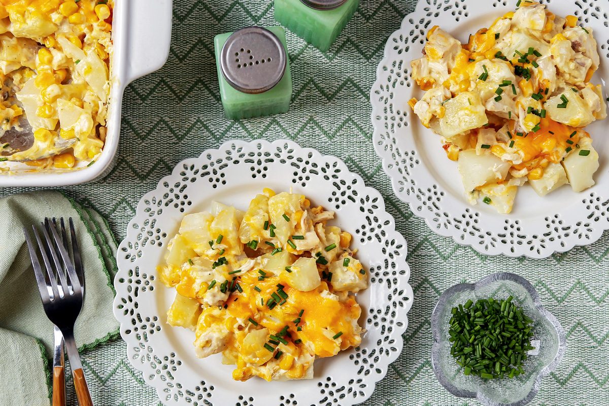 Overhead shot of Chicken and Potato Casserole; in a baking pan; served on plates; forks; napkin; salt and pepper shake; serving spoon; table cloth; marble surface;