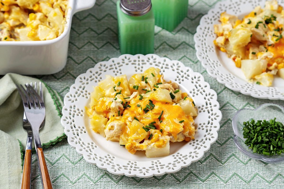High angle view shot of Chicken and Potato Casserole; in a baking pan; served on plates; forks; napkin; salt and pepper shake; serving spoon; table cloth; marble surface;