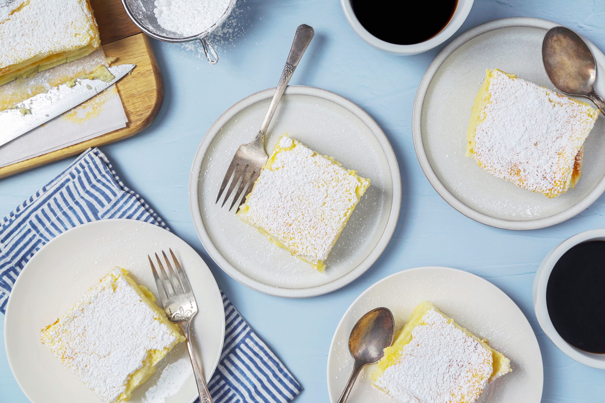 Four custard cakes served on individual white plates, dusted generously with powdered sugar