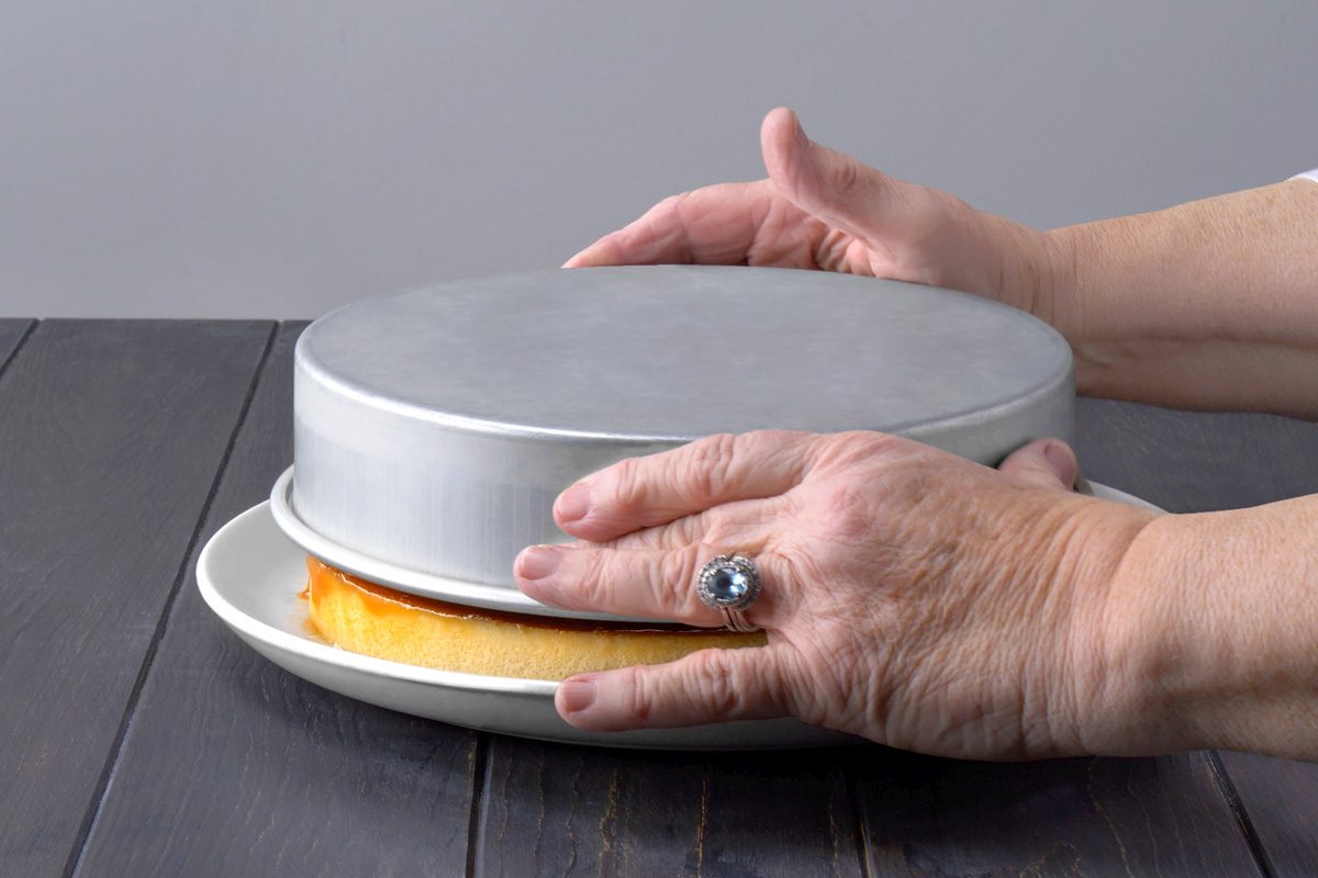 cake pan being flipped to transfer flan to serving dish