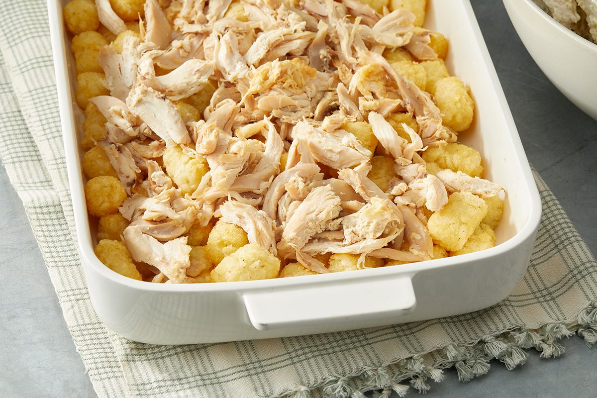 White casserole dish filled with shredded chicken and tater tots, placed on a checkered cloth.