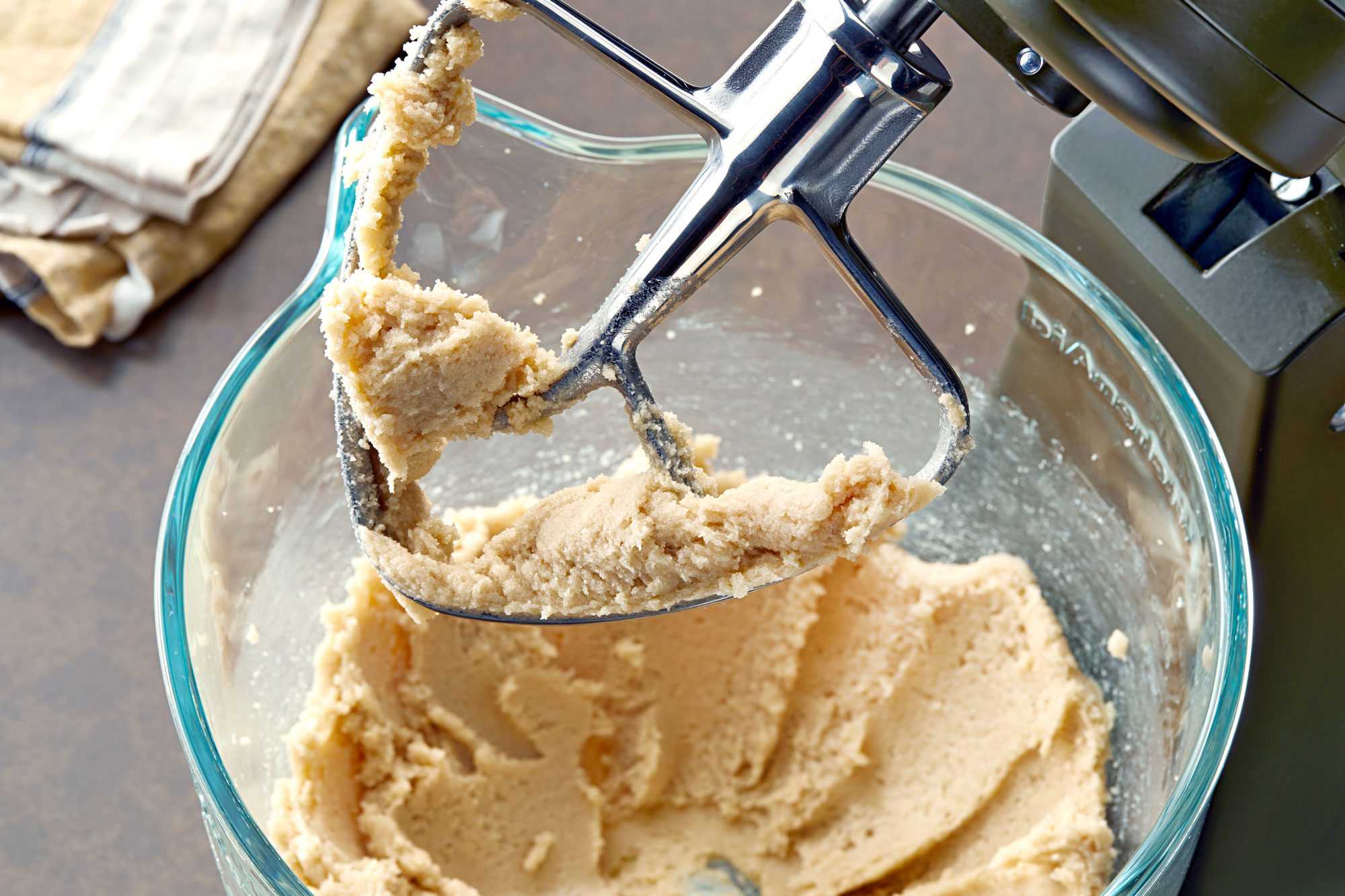 a close-up of a stand mixer with a dough hook attached to it; the hook is covered in a thick, creamy dough that looks like it's been recently mixed