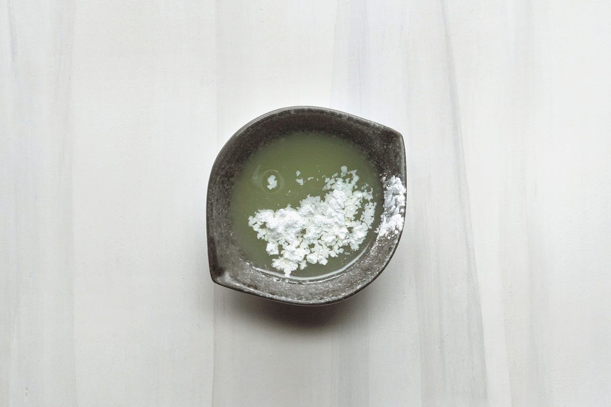 overhead shot of a small black bowl filled with a white liquid and white powder; the bowl is on a white background